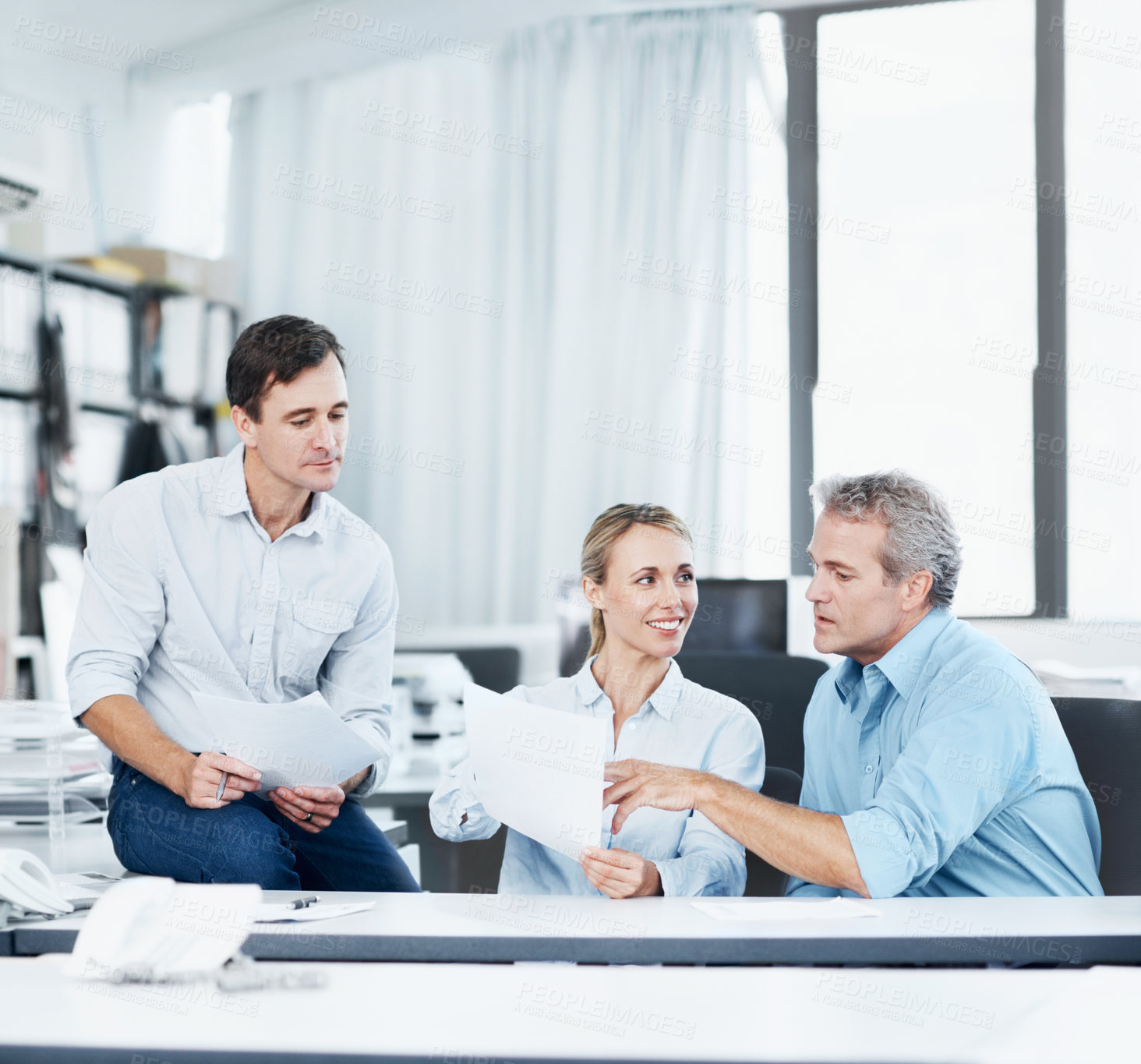 Buy stock photo Three coworkers talking while looking over some documents in the office