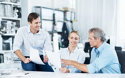 Buy stock photo Three colleagues talking while looking over some documents in the office