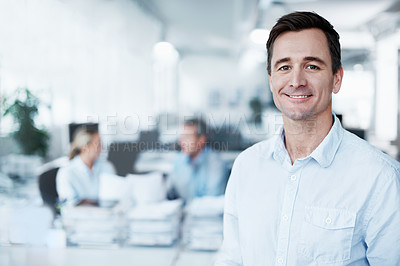 Buy stock photo Portrait of a handsome young man standing in the office while two coworkers converse in the background