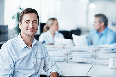 Buy stock photo Portrait of a handsome young man sitting in the office while two coworkers converse in the background