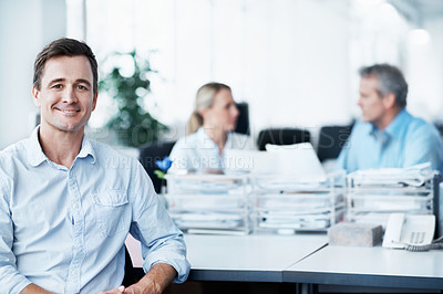 Buy stock photo Portrait of a handsome young man sitting in the office while two coworkers talk in the background