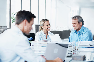 Buy stock photo A young businessman working on his laptop while his two colleagues talk in the background