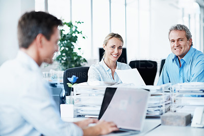 Buy stock photo Portrait of a two businesspeople sitting across from their colleague while he works on his laptop