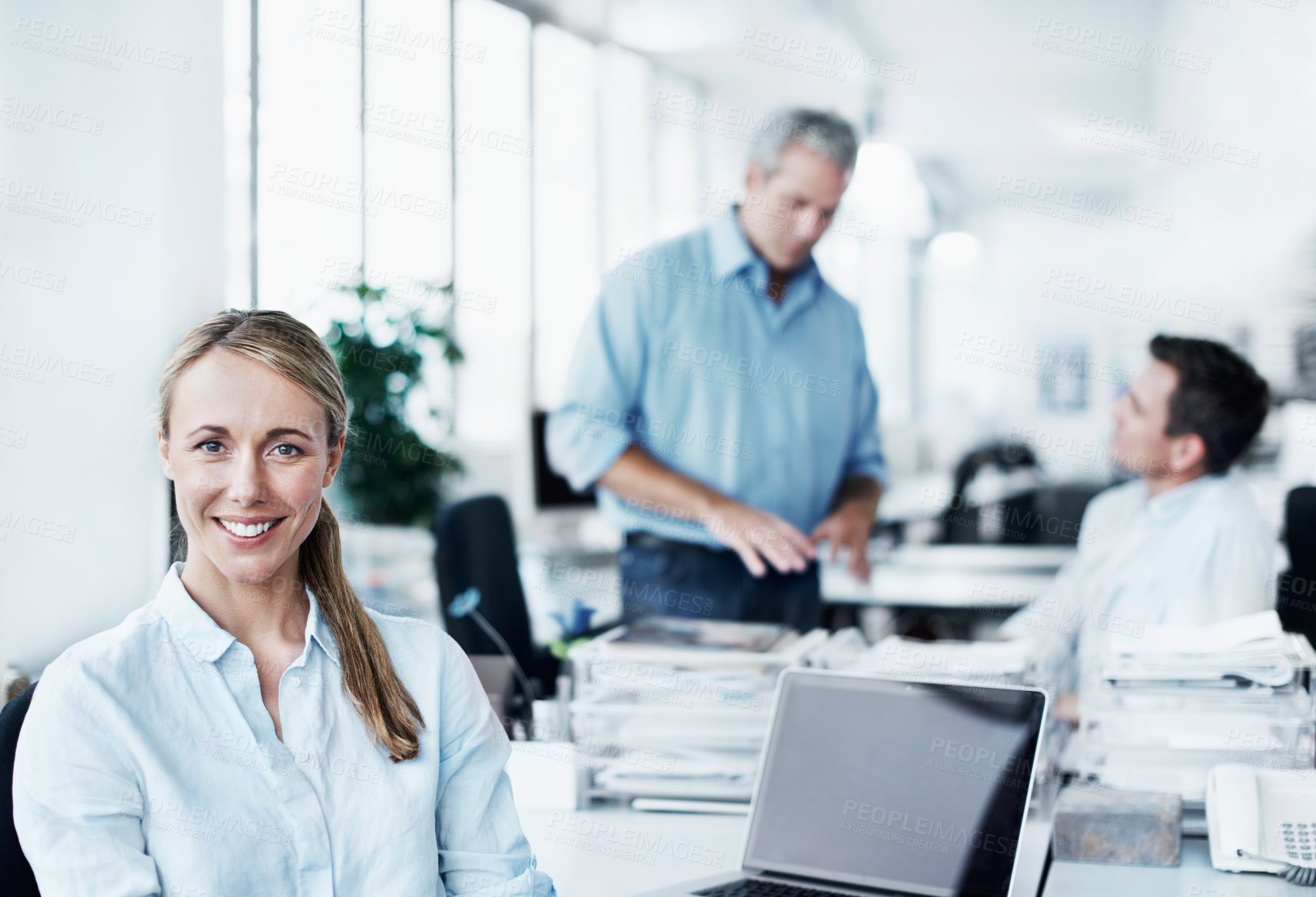 Buy stock photo Portrait of an attractive young businesswoman sitting at her desk with her coworkers in the background