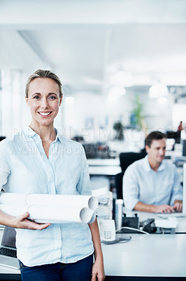 Buy stock photo Portrait of a beautiful young businesswoman holding plans with her colleagues in the background