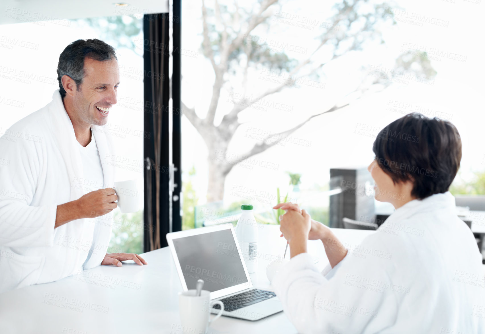 Buy stock photo Couple, happy and laptop in kitchen with coffee, travel planning and excited for anniversary trip. Man, woman and tech in home for vacation discussion, resort website and smile with drink for bonding