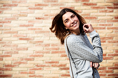 Buy stock photo Shot of a young woman posing against a brick wall outdoors
