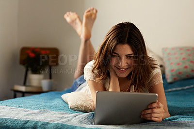Buy stock photo Shot of a young woman relaxing with a digital tablet on her bed