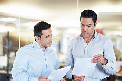Buy stock photo Shot of two colleagues discussing paperwork while standing in an office