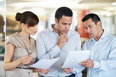 Buy stock photo Shot of three colleagues discussing paperwork while standing in an office