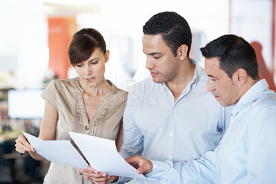 Buy stock photo Shot of three colleagues discussing paperwork while standing in an office