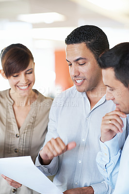 Buy stock photo Shot of three colleagues discussing paperwork while standing in an office