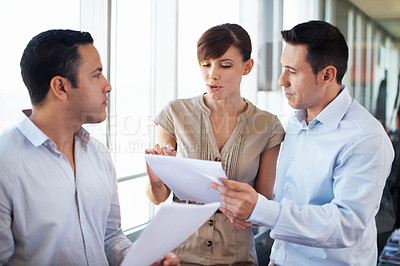 Buy stock photo Shot of three colleagues discussing paperwork while standing in an office