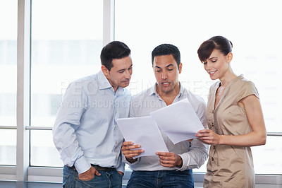 Buy stock photo Shot of three colleagues discussing paperwork while standing in an office