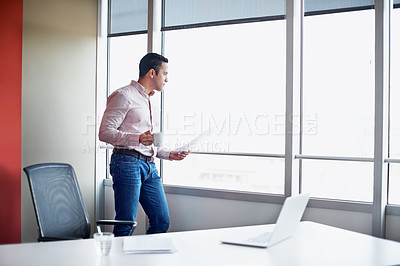 Buy stock photo Shot of a businessman holding paperwork while standing by an office window