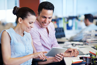 Buy stock photo Shot of two coworkers using a digital tablet while sitting at their desks in an office