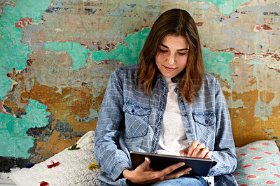 Buy stock photo Shot of a young woman relaxing with a digital tablet on her bed