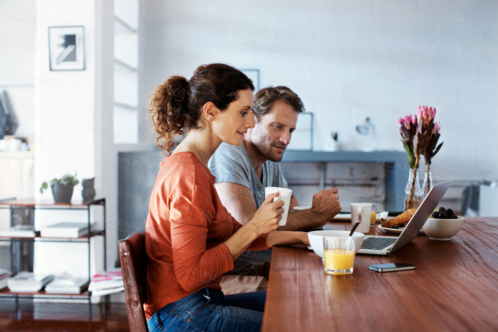 Buy stock photo Shot of a couple sitting at the dining table eating breakfast and using a laptop
