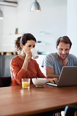 Buy stock photo Shot of a couple sitting at the dining table eating breakfast and using a laptop
