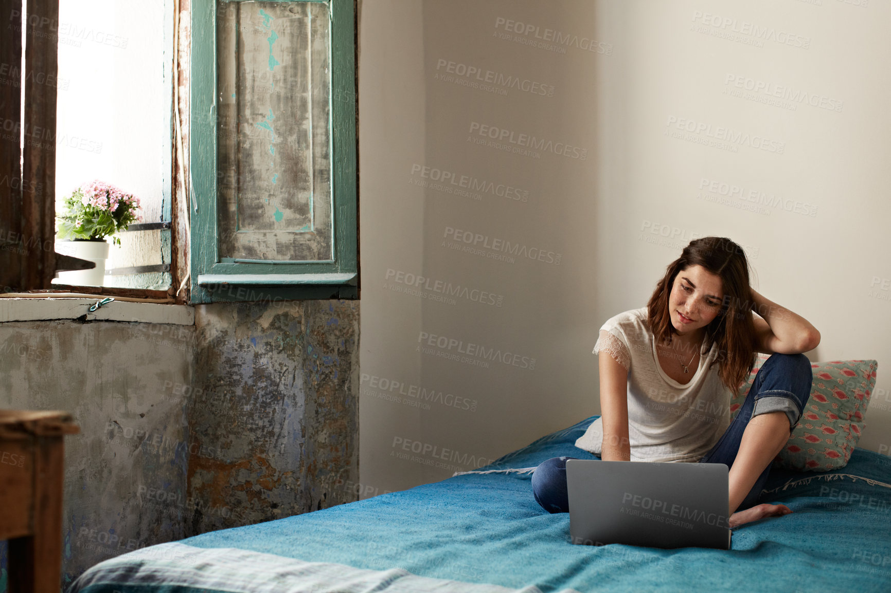 Buy stock photo Shot of a young woman sitting on her bed using a laptop