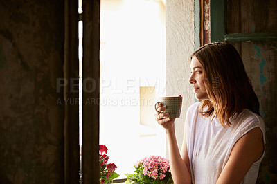Buy stock photo Shot of a young woman drinking a cup of coffee while looking out of a window
