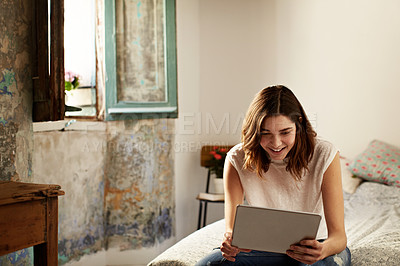 Buy stock photo Shot of a young woman sitting on her bed using a digital tablet