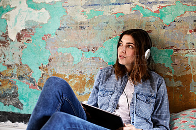Buy stock photo Shot of a young woman sitting on her bed listening to music on a digital tablet