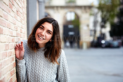 Buy stock photo Portrait of a smiling young woman leaning against a brick wall outside