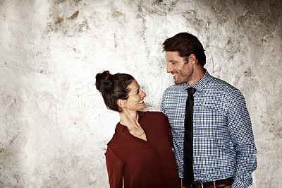 Buy stock photo Shot of an affectionate couple looking at each other while standing against a wall