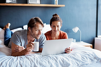 Buy stock photo Shot of a smiling couple lying in bed together using a laptop