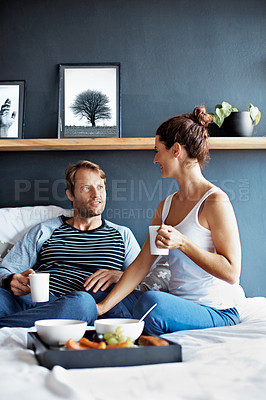 Buy stock photo Shot of a content couple sitting in bed together eating breakfast