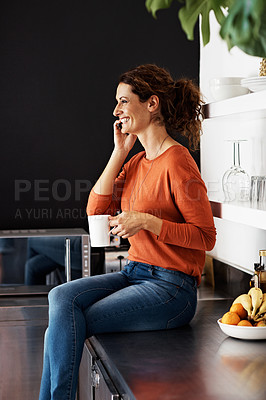 Buy stock photo Shot of a woman sitting on her kitchen counter drinking a coffee and talking on the phone