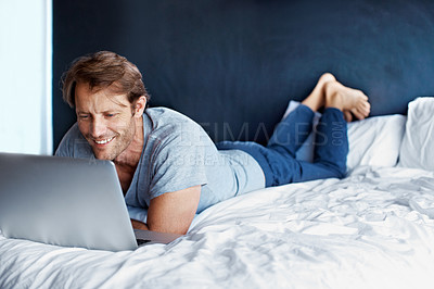 Buy stock photo Shot of a mature man lying on his bed using a laptop