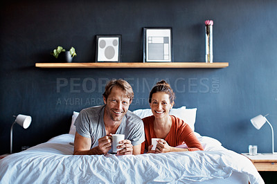 Buy stock photo Portrait of a smiling mature couple lying on their bed drinking coffee