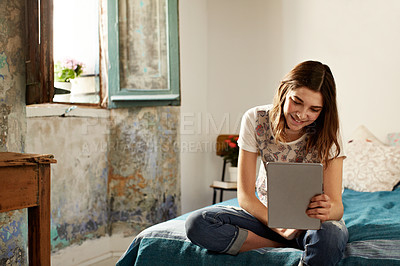 Buy stock photo Shot of a young woman using a digital tablet while sitting on her bed