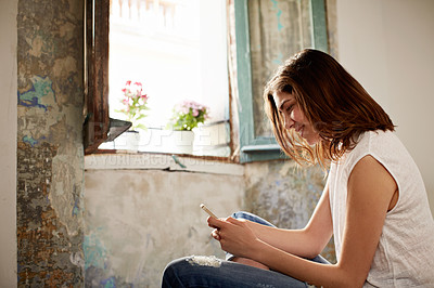 Buy stock photo Shot of a young woman using a cellphone while sitting on her bed