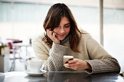 Buy stock photo Shot of a young woman using a cellphone while sitting in a cafe