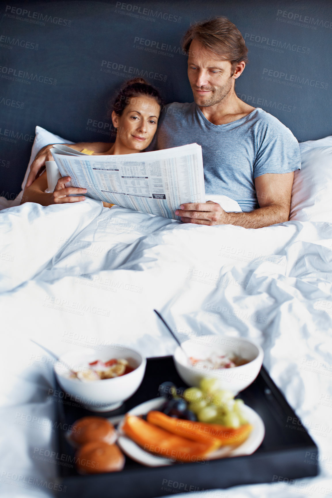 Buy stock photo Shot of content couple reading the paper together and having breakfast in bed