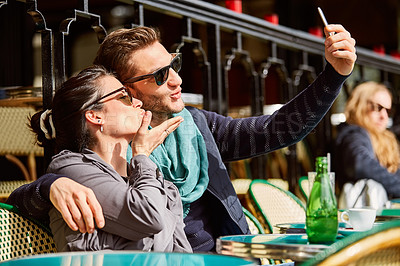 Buy stock photo Shot of a smiling couple talking a selfie while sitting together at a table at a sidewalk cafe