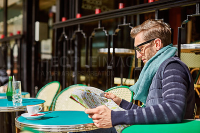 Buy stock photo Shot of a stylish young man reading a map while sitting at a table outside at a sidewalk cafe
