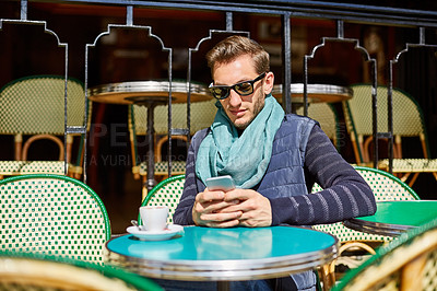 Buy stock photo Shot of a stylish young man using a cellphone while sitting at a table outside at a sidewalk cafe