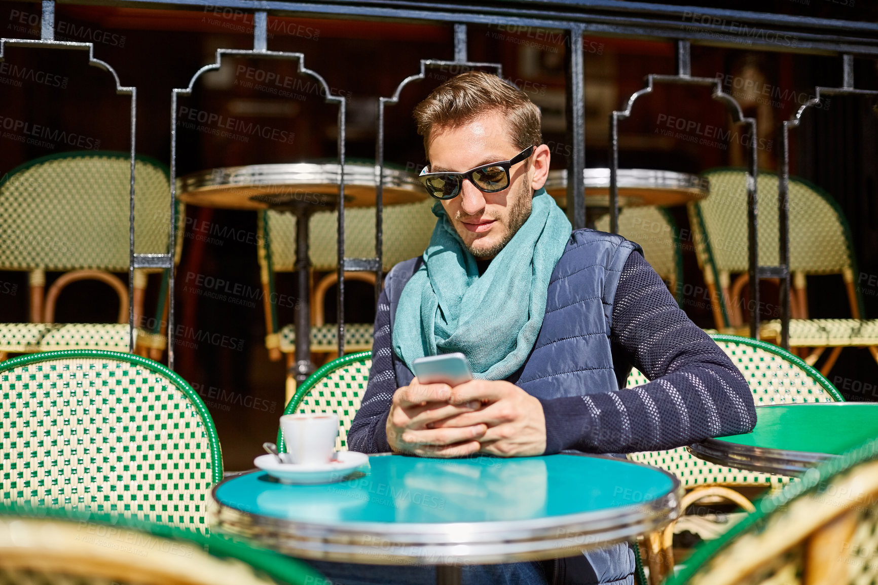 Buy stock photo Shot of a stylish young man using a cellphone while sitting at a table outside at a sidewalk cafe