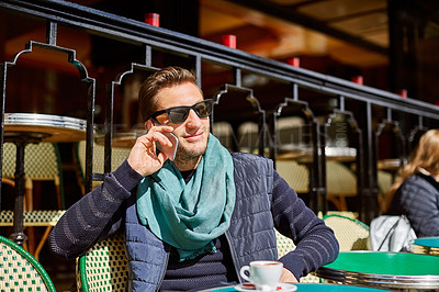 Buy stock photo Shot of a stylish young man talking on a cellphone while sitting at a table outside at a sidewalk cafe