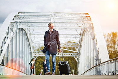 Buy stock photo Shot of a mature man pulling a suitcase while walking over a bridge in the city