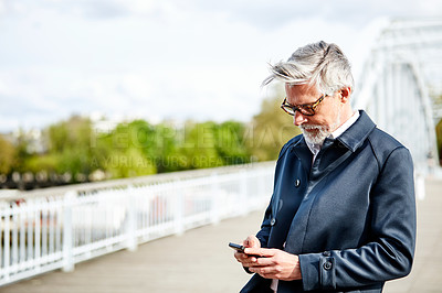 Buy stock photo Shot of a handsome mature man using a cellphone while standing on a bridge in the city