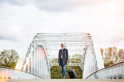 Buy stock photo Shot of a mature man pulling a suitcase while walking over a bridge in the city