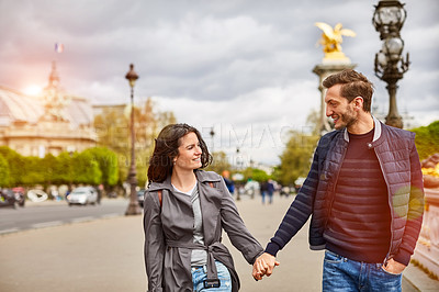 Buy stock photo Shot of a smiling young couple walking hand in hand together in the streets of Paris