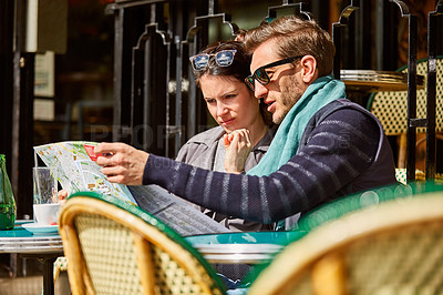Buy stock photo Shot of a young couple sitting together at a table at a sidewalk cafe in Paris reading a map