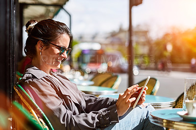 Buy stock photo Shot of a smiling young woman sitting at a sidewalk cafe in Paris using a digital tablet