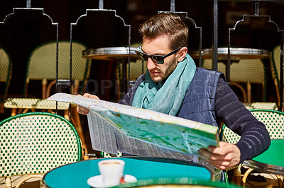 Buy stock photo Shot of a young man reading a map while sitting at a table at a sidewalk cafe